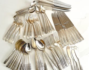 May include: A set of vintage silverware in a silver finish. The set includes forks, knives, spoons, and butter knives. The silverware has an ornate design.