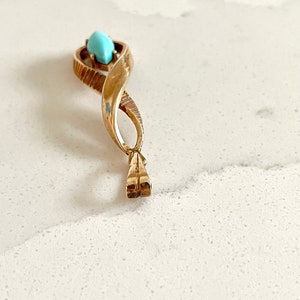 May include: A gold pendant with a turquoise stone in the center. The pendant is shaped like a twisted rope.
