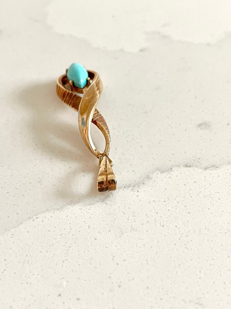 May include: A gold pendant with a turquoise stone in the center. The pendant is shaped like a twisted rope.