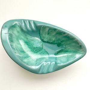 May include: A light blue ceramic ashtray with a swirl pattern. The ashtray is shaped like a leaf and has a wide, shallow bowl.