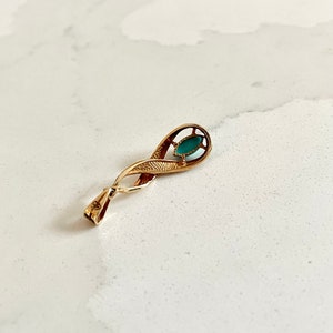 May include: A gold pendant with a green stone set in a delicate, twisted design.
