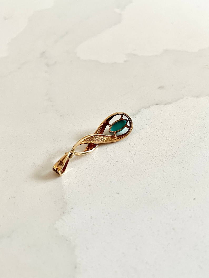 May include: A gold pendant with a green stone set in a delicate, twisted design.