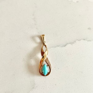 May include: A gold pendant with a turquoise stone in the center. The pendant is shaped like a twisted rope.