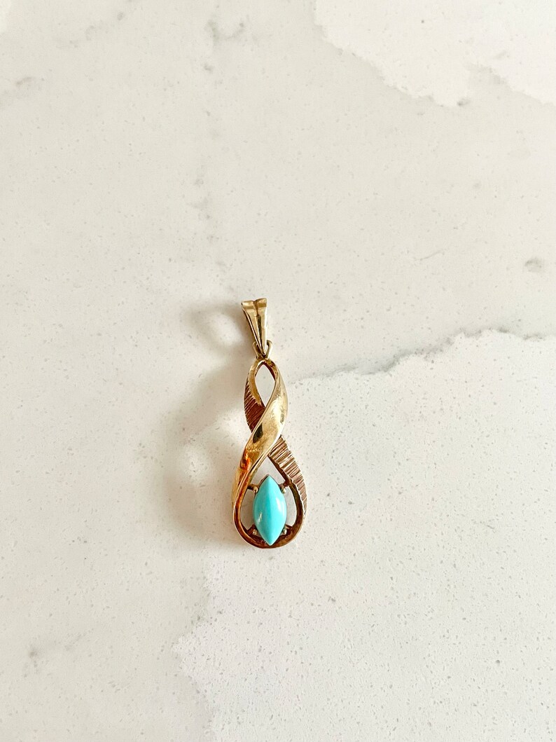 May include: A gold pendant with a turquoise stone in the center. The pendant is shaped like a twisted rope.