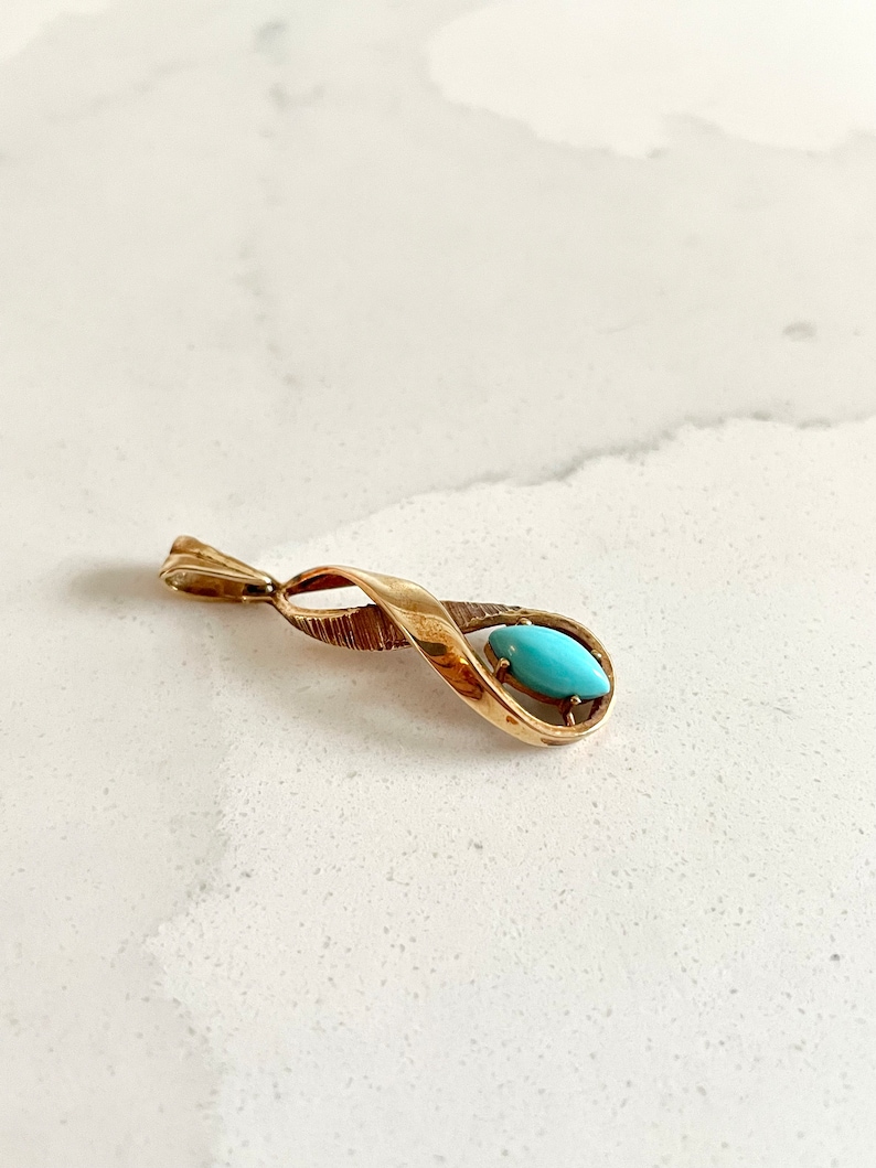 May include: A gold pendant with a turquoise stone set in a twisted design.