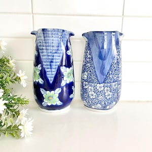 May include: Two blue and white ceramic vases with floral patterns. The vase on the left has a blue and white geometric pattern with green and yellow flowers. The vase on the right has a white floral pattern on a blue background.