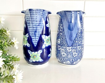 May include: Two blue and white ceramic vases with floral patterns. The vase on the left has a blue and white geometric pattern with green and yellow flowers. The vase on the right has a white floral pattern on a blue background.