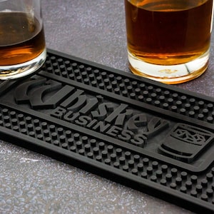 May include: Black bar mat with the text "Whiskey Business" and a stylized image of a glass of whiskey. The mat has a textured surface with small raised dots.