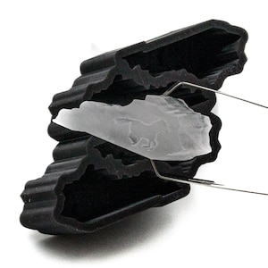 May include: A black silicone mold shaped like a mountain range with a clear ice cube inside. The ice cube is being lifted out of the mold with a metal tool.