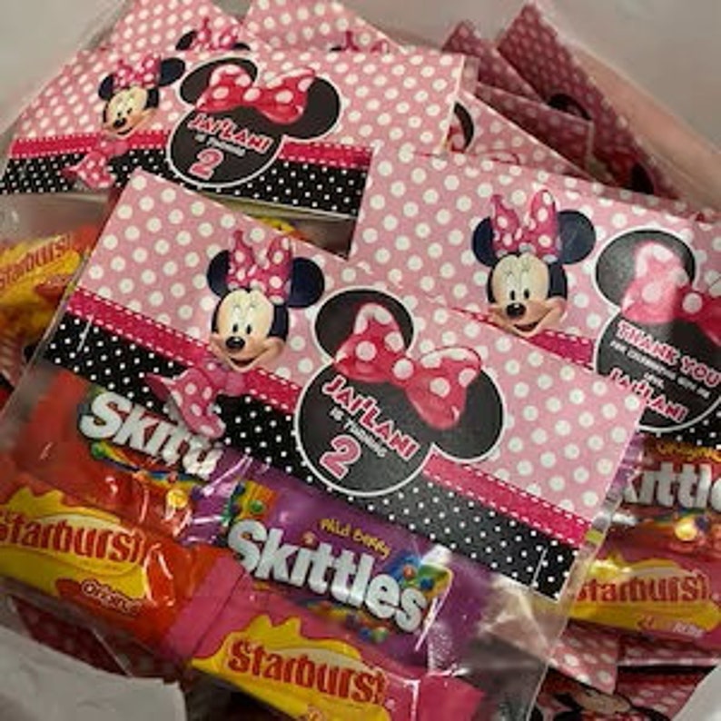 K&ouml;nnte beinhalten: Rosa und schwarze Partytaschen mit Minnie Mouse-Motiv, gef&uuml;llt mit S&uuml;&szlig;igkeiten. Die Taschen haben einen Minnie Mouse-Kopf mit einer roten Schleife und den Text "JAFILANI wird 2" darauf gedruckt.