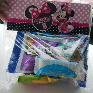 K&ouml;nnte beinhalten: Eine rosa und schwarze Partyt&uuml;te mit einem Minnie Mouse-Charakter und dem Text "Anya ist 3" auf der Vorderseite. Die T&uuml;te ist gef&uuml;llt mit verschiedenen kleinen Snacks und Leckereien.