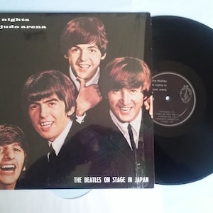 May include: A black and white vinyl record album cover featuring a photo of the Beatles. The album title is "Five Nights in a Judo Arena" and the text "The Beatles on Stage in Japan" is at the bottom of the cover.