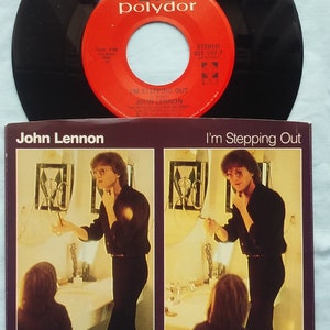 May include: A black vinyl record with a red label that says "Polydor" and "I'm Stepping Out" by John Lennon. The record is on a white surface with a picture of John Lennon in a black suit and a young child in a black shirt.