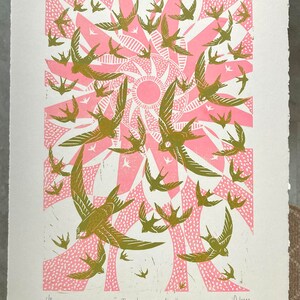 May include: A print featuring a flock of birds in flight, rendered in shades of olive green and pink. The birds are set against a stylized sunburst design. The text "The sky was alive" is at the bottom.