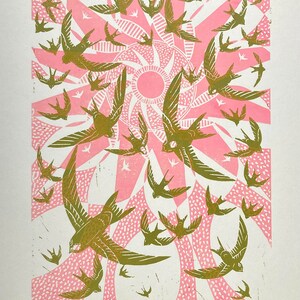 May include: A print featuring a flock of birds in flight, rendered in shades of olive green and pink. The birds are set against a stylized sunburst design. The text "The sky was alive" is at the bottom.