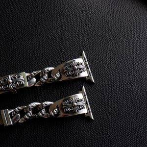 May include: Two silver watch bands with ornate, symmetrical designs. The bands feature a chain-link style and decorative clasps. The watch bands are displayed against a dark, textured background.
