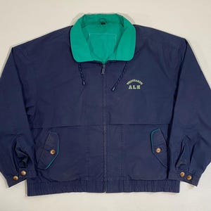 May include: Navy blue jacket with a green collar and trim. The jacket has a zipper closure, two front pockets, and the text "RICHARDSON ALE" embroidered on the chest. The jacket has a drawstring at the collar and cuffs with button closures.