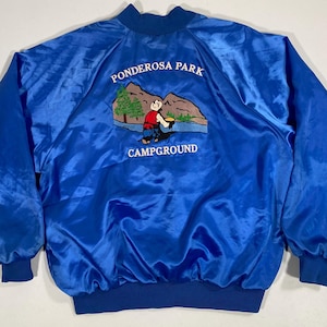 May include: A vibrant blue satin jacket with a crew neck and elastic cuffs. The back features an embroidered design with the words "Ponderosa Park Campground" and a cartoon illustration of a person near a lake and mountains.