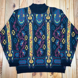 May include: A navy blue patterned jumper with a mock neck. The design includes yellow, teal, and purple floral and geometric motifs. The jumper is made of a soft, knitted material.