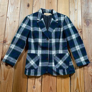 May include: A long-sleeve blazer featuring a dark green, navy blue, and white plaid pattern. The garment includes a notched lapel, three front buttons for closure, and two large patch pockets on the lower front. The interior is lined in black.