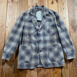 May include: A long-sleeve blazer featuring a blue, tan, and white plaid pattern. The garment includes a notched lapel, three dark brown buttons down the front, one chest pocket, and two large patch pockets at the waist with a light gray interior lining.