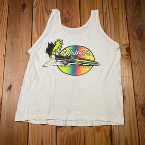 Pu&ograve; includere: Canotta bianca con una grafica colorata di un'auto da drag racing, palme e la scritta "NHRA Championship Drag Racing" in un cerchio arcobaleno. La canotta &egrave; realizzata in un materiale morbido e leggero.