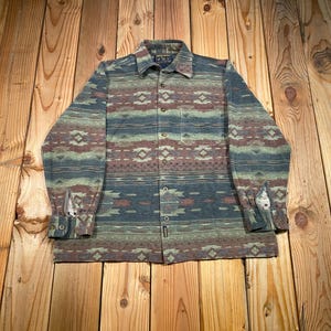 May include: A button-down shirt with a Southwestern-inspired pattern in shades of blue, green, and brown. The long-sleeved shirt features a collared neckline, a chest pocket, and buttoned cuffs. The shirt is made of a soft, textured fabric.