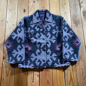 May include: A long-sleeve button-up jacket featuring a dark gray and light gray geometric pattern with maroon and teal accents. The jacket has a standard collar, a dark interior lining, and a visible brand label at the inner neckline.