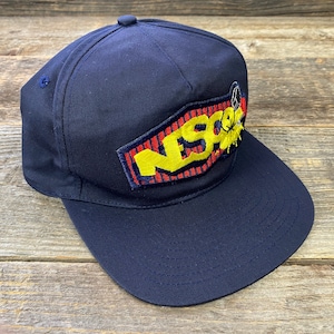 May include: A navy blue baseball cap with a yellow, red, and black embroidered patch that says "NESO" on it.