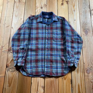May include: A long-sleeve button-down shirt featuring a plaid pattern in shades of deep red, navy blue, and light blue. The shirt includes a standard collar, a single chest pocket on the left side, and buttoned cuffs on the sleeves.