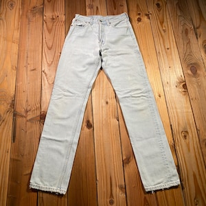 May include: A pair of light-wash blue denim jeans featuring a high-waisted fit, a button fly closure, five pockets, and straight-cut legs with a slightly distressed hemline. The denim fabric displays a faded, worn-in appearance throughout the garment.