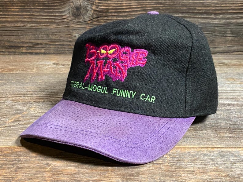 May include: Black baseball cap with a purple brim. The cap features the text "Boogie Man" in pink and "Federal-Mogul Funny Car" in green.