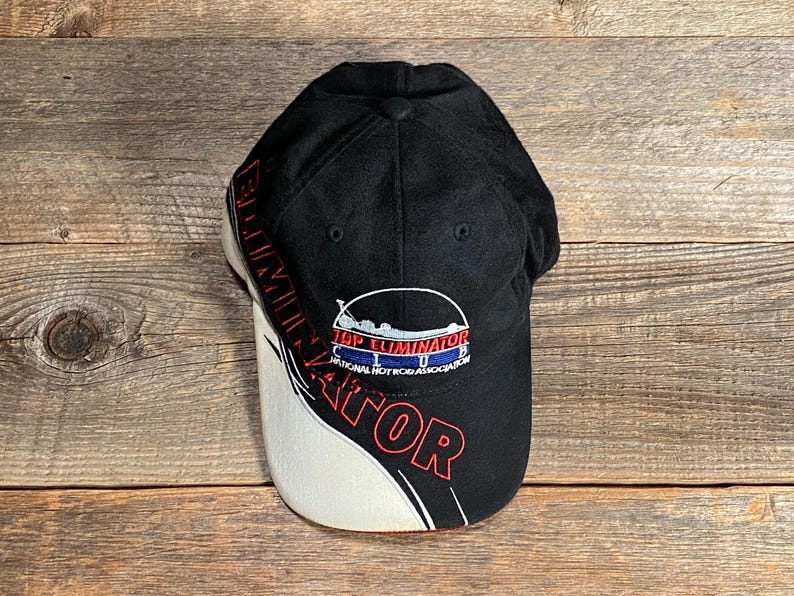 May include: Black baseball cap with the words "Top Eliminator" in red and white. The cap has a white and black curved design on the side. The cap also has the words "National Hot Rod Association" on the front.