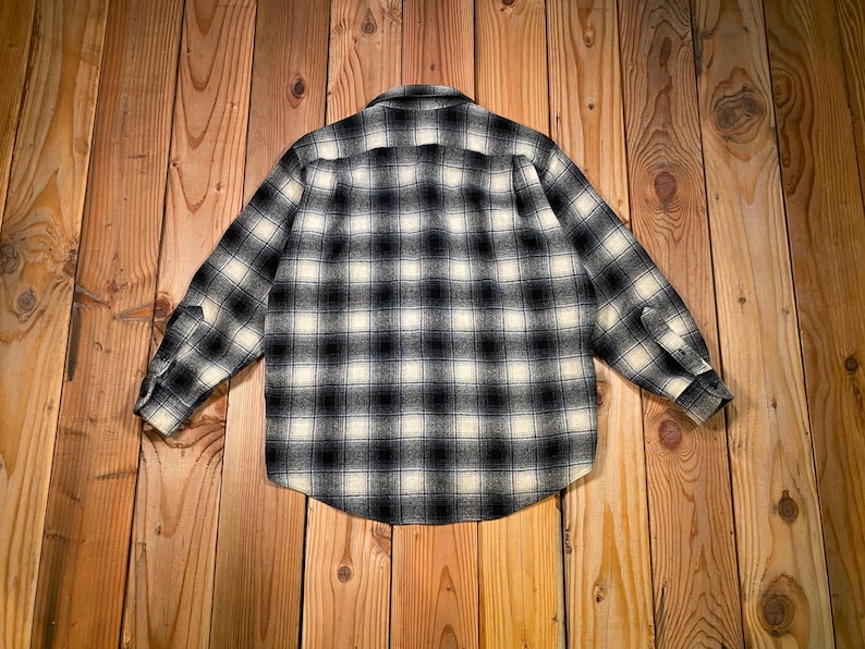 May include: A black and white checked button-down shirt. The shirt features long sleeves and a standard collar. The check pattern is composed of black and cream squares. The shirt is made from a soft, woven material.