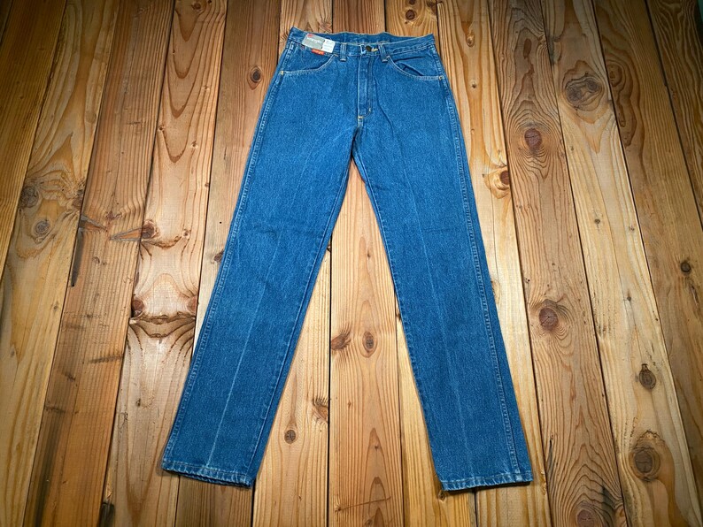May include: Blue denim jeans with a classic five-pocket design. The jeans have a straight leg cut and a button and zipper closure. The denim has a medium wash with subtle fading and a red and white tag on the back pocket.