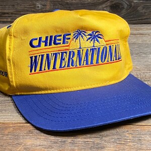May include: A yellow and blue baseball cap with the text "CHIEF WINTERNATIONAL" in blue and red. The cap has a blue brim and a small American flag patch. The text "TOUR 994" is also visible.