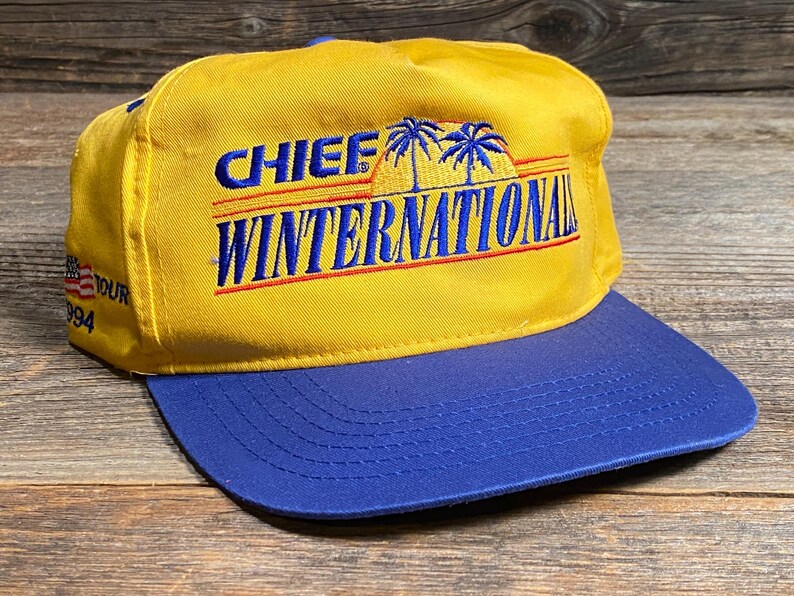 May include: A yellow and blue baseball cap with the text "CHIEF WINTERNATIONAL" in blue and red. The cap has a blue brim and a small American flag patch. The text "TOUR 994" is also visible.