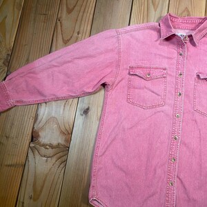 Puede incluir: Una camisa de manga larga con botones en tela de mezclilla rosa deste&ntilde;ida. La camisa presenta un cuello est&aacute;ndar, una tapeta de botones frontal completa y dos bolsillos en el pecho con solapas abotonadas. Las mangas tienen pu&ntilde;os abotonados.