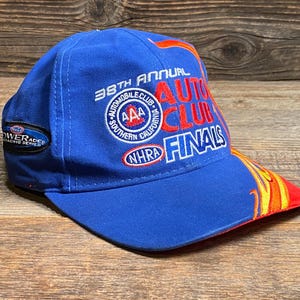 Puede incluir: Gorra de b&eacute;isbol azul con el texto "38th Annual Auto Club Finals" en rojo y blanco. La gorra presenta una visera curva con un dise&ntilde;o de llamas en rojo, amarillo y naranja. La gorra tambi&eacute;n tiene un parche que dice "Powerade Racing Series".