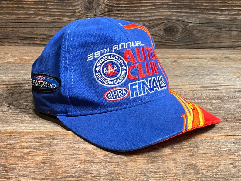 Puede incluir: Gorra de b&eacute;isbol azul con el texto "38th Annual Auto Club Finals" en rojo y blanco. La gorra presenta una visera curva con un dise&ntilde;o de llamas en rojo, amarillo y naranja. La gorra tambi&eacute;n tiene un parche que dice "Powerade Racing Series".