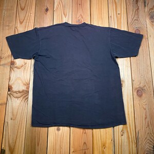Puede incluir: Una camiseta de manga corta de color azul marino oscuro s&oacute;lido con cuello redondo. La prenda se muestra extendida, revelando la parte posterior lisa de la camiseta sin gr&aacute;ficos, patrones ni texto visibles en la superficie de la tela.