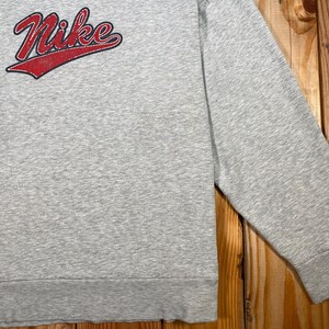 Puede incluir: Una sudadera gris con el logo de Nike en rojo con un acento rojo. La camisa de manga larga est&aacute; hecha de un material suave y tiene un pu&ntilde;o acanalado en la mu&ntilde;eca.