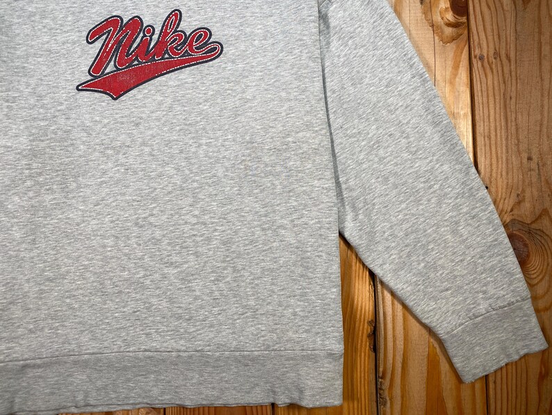 Puede incluir: Una sudadera gris con el logo de Nike en rojo con un acento rojo. La camisa de manga larga est&aacute; hecha de un material suave y tiene un pu&ntilde;o acanalado en la mu&ntilde;eca.