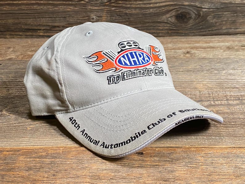 May include: A light grey baseball cap with the NHRA Top Eliminator Club logo in red, orange, and blue. The cap also displays "40th Annual Automobile Club of Southern California" and "Members Only" text.