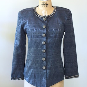 May include: A dark navy blue long-sleeve jacket featuring a tonal jacquard pattern, a round neckline adorned with silver-toned studs, and a front button closure with six matching circular buttons. The sleeve cuffs are also detailed with silver-toned studs.