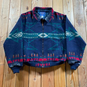 May include: A navy blue zip-up jacket featuring a geometric pattern in teal, red, and cream. The jacket has a fold-down collar, long sleeves with ribbed cuffs, a ribbed hem, and two front pockets. The Pendleton brand label is visible at the neck.
