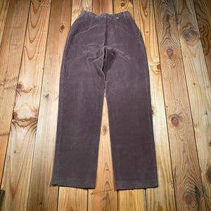 May include: Brown corduroy pants with a high waist and straight leg. The pants are made of a soft, ribbed fabric and have a classic design. The pants are laid flat on a wooden surface.
