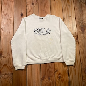 May include: A white long-sleeve crewneck sweatshirt featuring the text POLO JEANS COMPANY embroidered in black on the chest. The garment has ribbed cuffs and a ribbed hem, with a standard fit and a classic round neckline design.