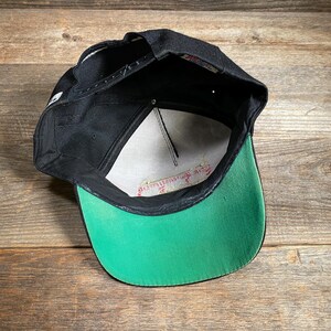 May include: Black baseball cap with a green brim and white mesh interior. The cap has a snapback closure and a small white logo on the side. The brim is a bright green color, and the cap is made of a durable material.