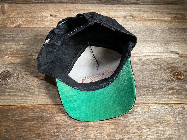 May include: Black baseball cap with a green brim and white mesh interior. The cap has a snapback closure and a small white logo on the side. The brim is a bright green color, and the cap is made of a durable material.
